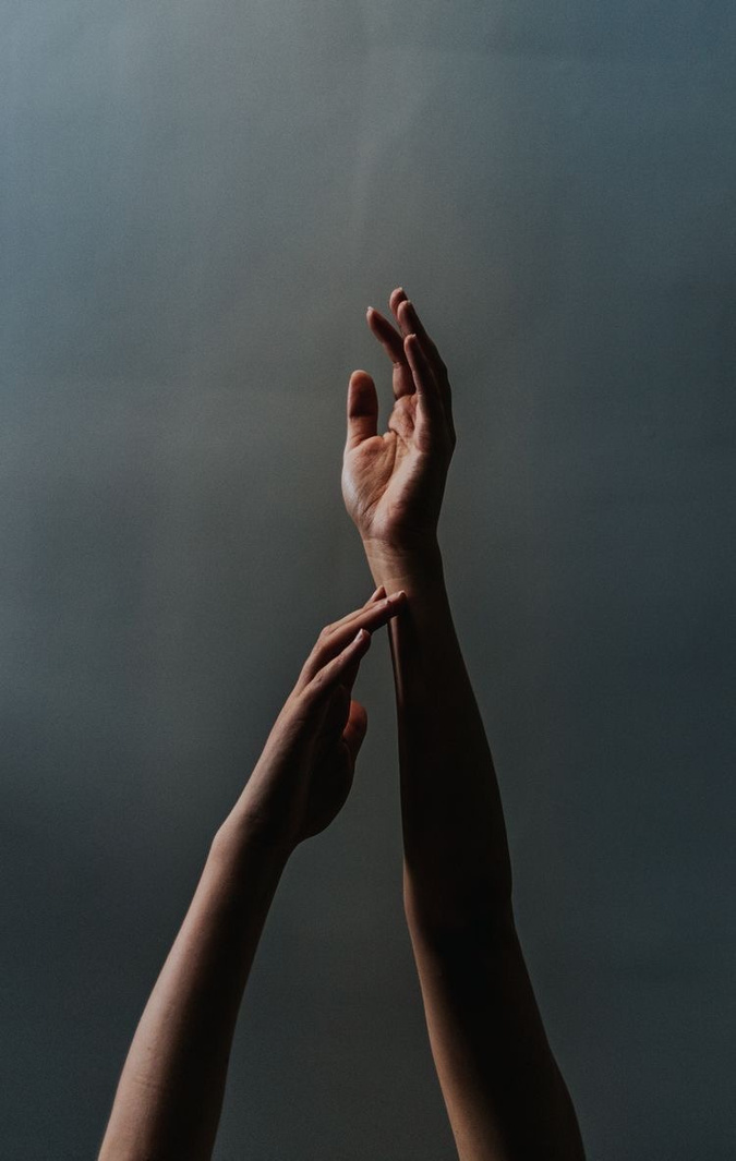 Two arms reaching upwards against a moody blue-grey background
