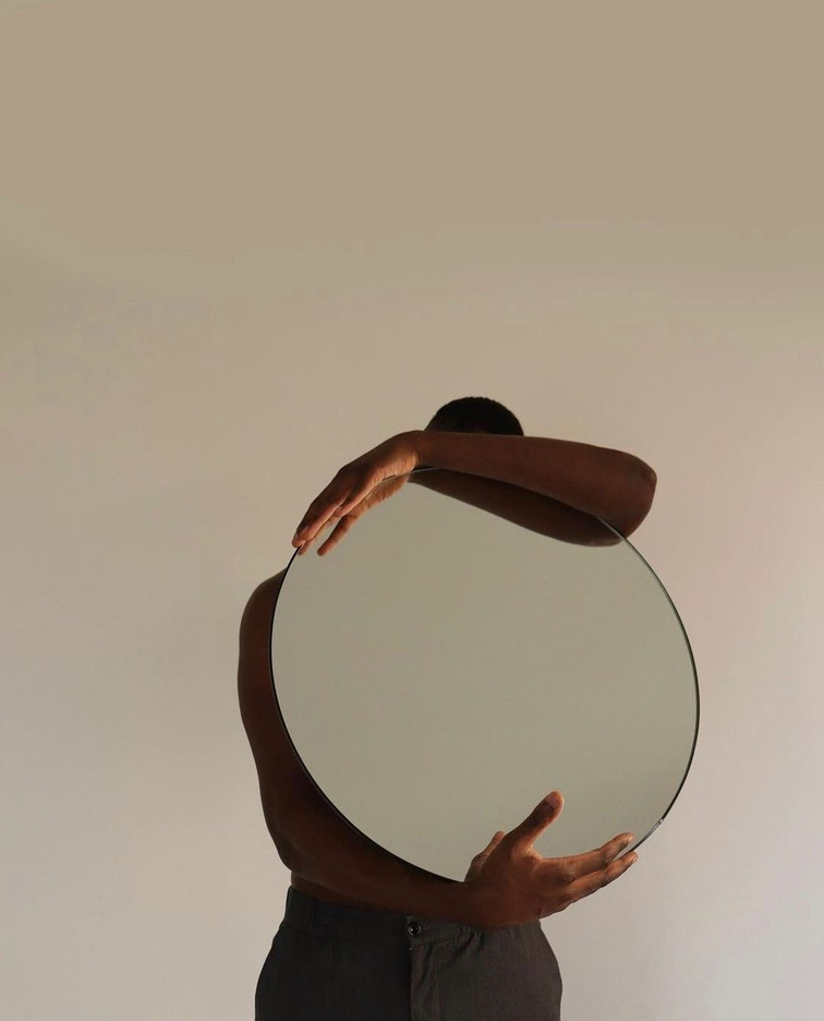 Figure holding a circular mirror in front of their face