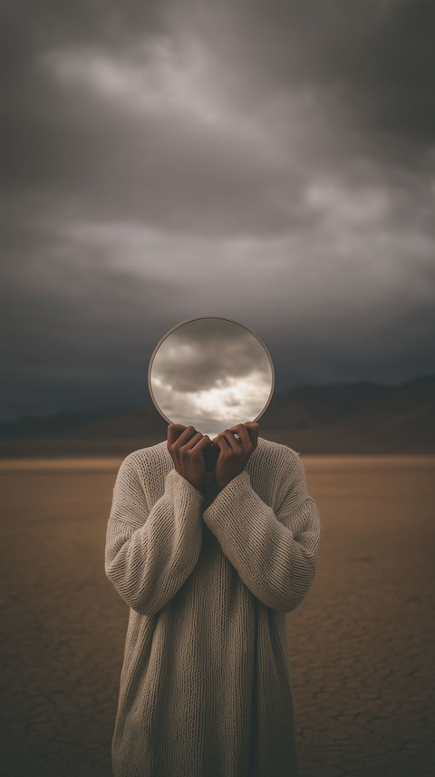 Figure holding a reflective sphere in a dramatic landscape
